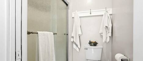 A bathroom with a glass shower door, a toilet, and a towel rack with multiple towels.