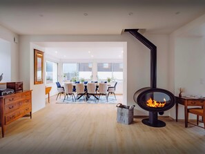 Ein modernes Wohnzimmer mit Kamin, einer Essecke mit Tisch und Stühlen sowie einer Holzkommode.