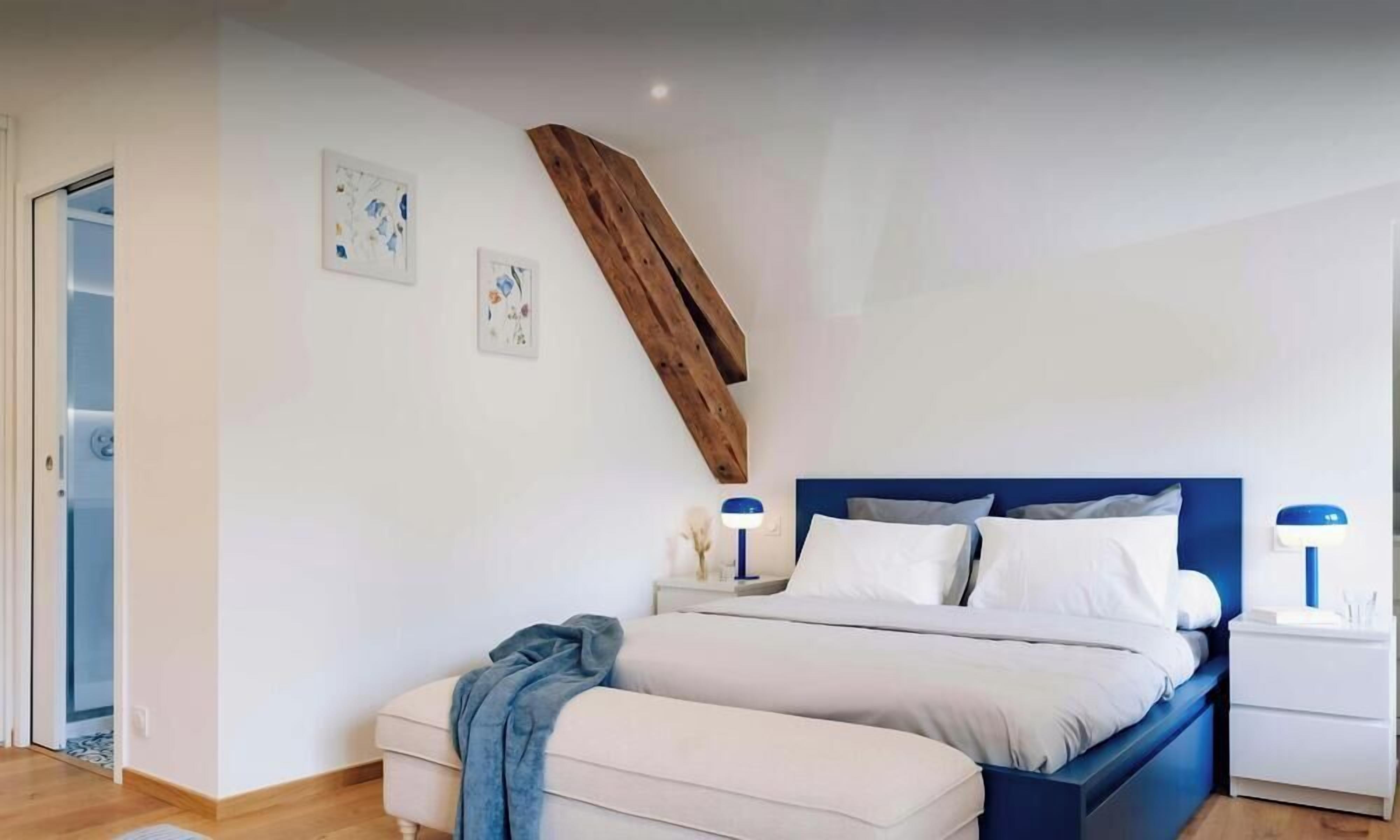 Een slaapkamer met een bed, nachtkastjes, een nachtkast en een houten balk, plus een deur.