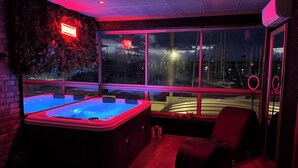 A room with a large window, a hot tub, and a view of boats and water.