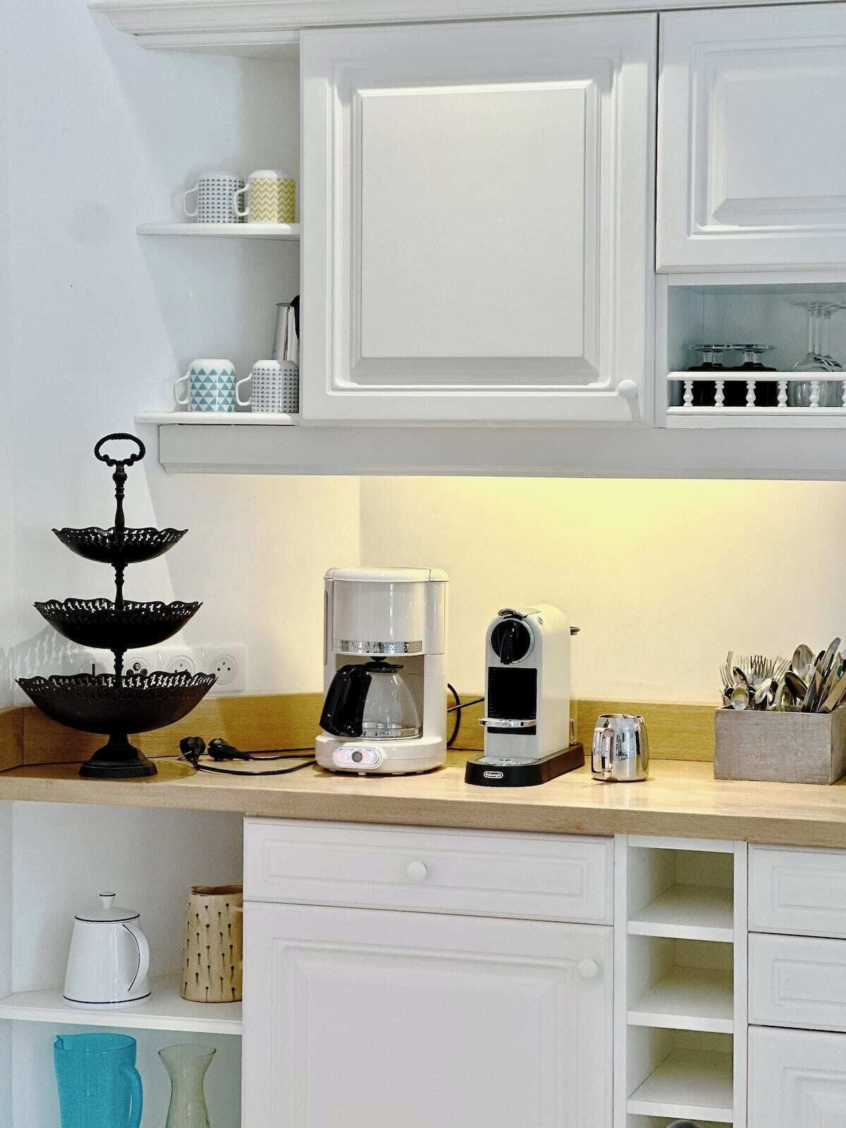 A kitchen with white cabinetry, a coffee maker, a kettle, and a utensil holder.