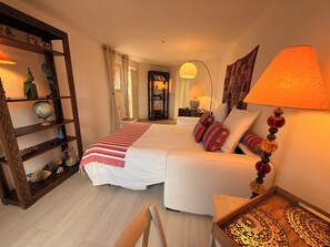 A bedroom with a bed, a sofa, a wooden shelf with decorative items, a lamp, and a patterned tray.