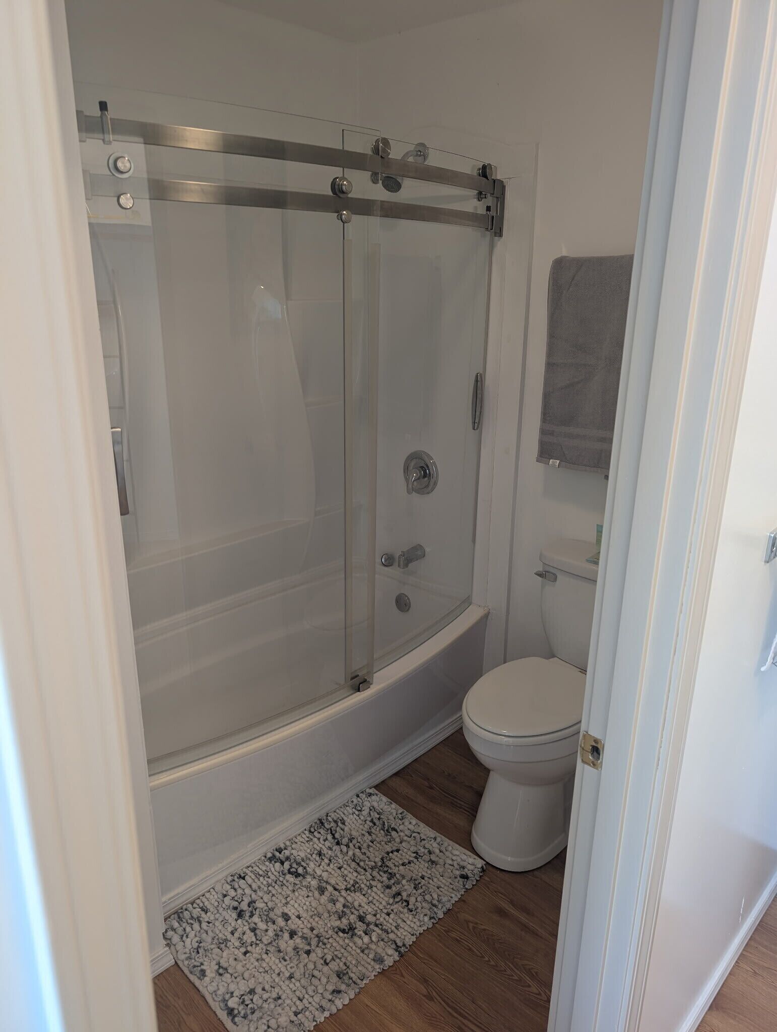 Une salle de bain avec une douche à parois de verre, des toilettes et un petit tapis sur le sol.