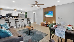 Une cuisine moderne avec un coin bar, une table à manger pour quatre personnes et un espace salon comprenant un canapé et des fauteuils.