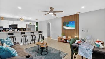 A modern kitchen with a bar area, a dining table set for four, and a living area with a sofa and chairs.