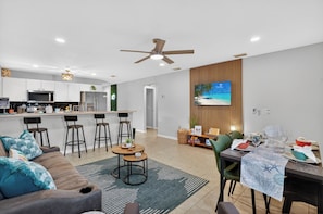 A modern kitchen with a bar area, a dining table set for four, and a living area with a sofa and chairs.