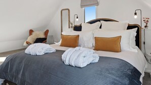 A modern bedroom with a large bed, multiple pillows, a fluffy animal head on the chair, and a window with a view.