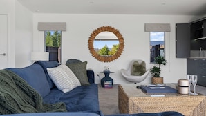 A modern living room with a blue sofa, a round mirror, and a view of the outdoors through large windows.
