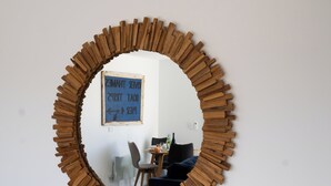 A circular mirror with a wooden frame, a blue sign with text, and a dining area with chairs and a table.