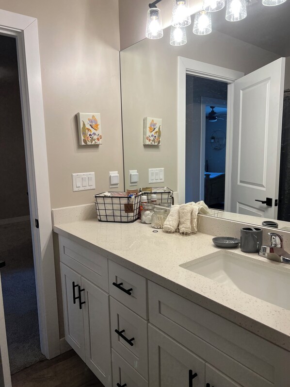 Un baño moderno con un espejo grande, armarios blancos, una encimera con artículos de aseo y decoración de mariposas en la pared.