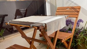 A wooden outdoor seating area with a table and chairs, a glass partition, and potted plants.
