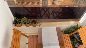 A wooden table and chairs set on a balcony with potted plants and a view of a building.