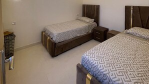 A modern bedroom with two beds, a small bedside table, and a trash bin.