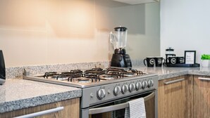 Eine moderne Küche mit Edelstahlherd, Granitarbeitsplatten, Holzschränken und einem eingebauten Backofen.