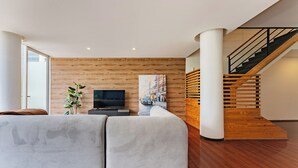 Ein modernes Wohnzimmer mit einer großen Eckcouch, einem Flachbildfernseher, einer Holzverkleidung und einer Treppe.