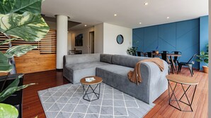 Ein modernes Wohnzimmer mit einem grauen Ecksofa, einem runden Couchtisch und einem Essbereich mit blauer Akzentwand.