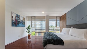 Ein modernes Hotelzimmer mit einem großen Bett, einem Stadtbildgemälde, einer Zimmerpflanze und großen Fenstern mit Blick auf die Stadt.