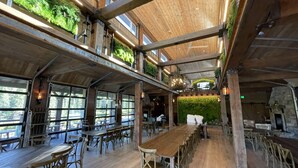 Ein geräumiges Restaurant mit hohen Decken, Holzbalken und großen Fenstern. Tische und Stühle sind zum Essen angerichtet.