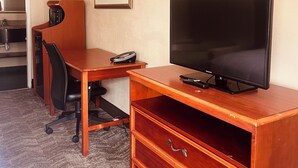 A hotel room with a wooden desk, a flat-screen TV, a chair, a small kitchenette, and a carpeted floor. - Stay-Well Inn  (Monroe)