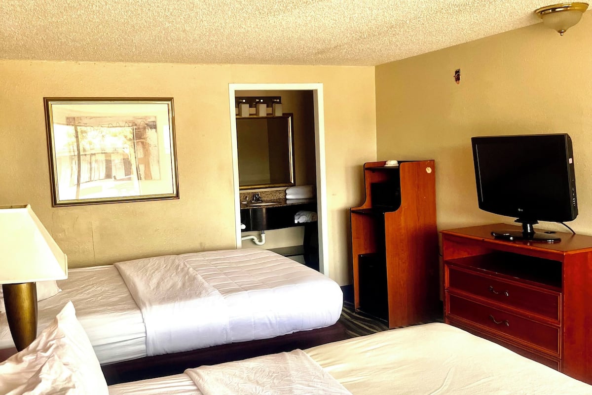 A hotel room with two beds, a TV, a desk, and a bathroom visible through an open door.