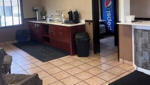 A kitchen with a refrigerator, microwave, and coffee maker. There is a trash can and a chair. - Stay-Well Inn  (Monroe)