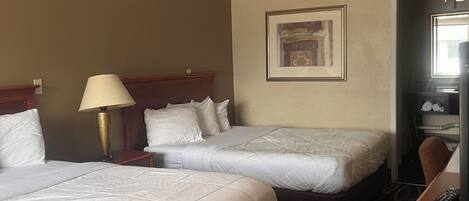 A hotel room with two beds, a desk, a lamp, and a framed picture on the wall.
