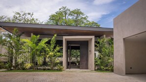 Un bâtiment moderne doté d’une entrée couverte, entouré d’une végétation luxuriante et bordé d’un chemin pavé.