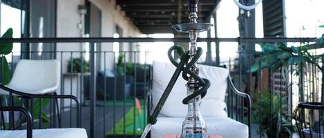 Een shisha op een houten tafel op een balkon met terras en uitzicht op een tuin.