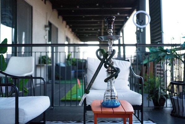 A hookah on a wooden table on a balcony with outdoor seating and a view of a garden.