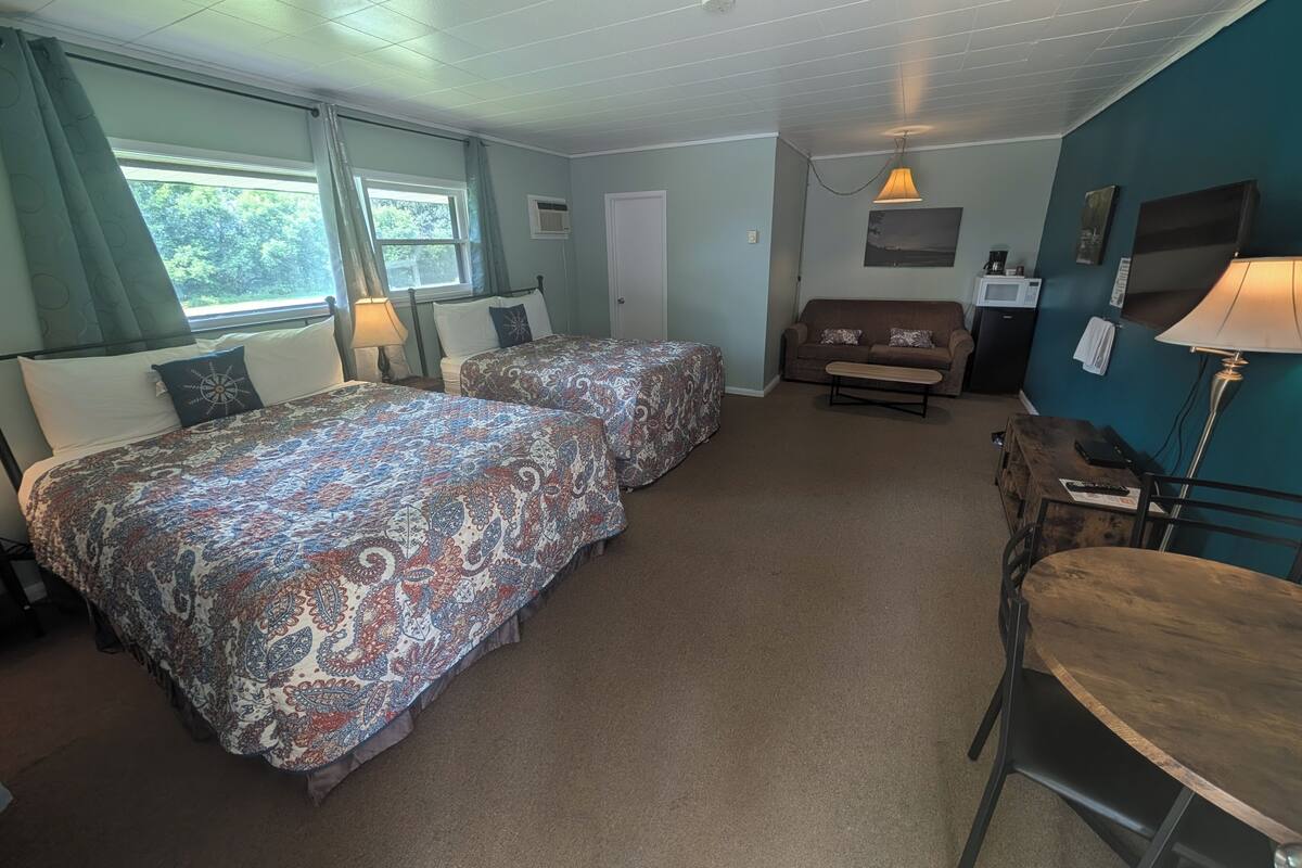 A room with two beds, a sofa, a table, and a lamp.