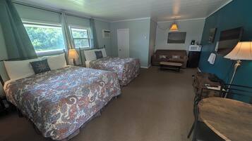 A room with two beds, a sofa, a table, and a lamp.