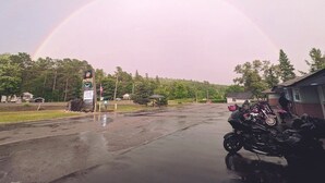 A parking area with a motorcycle, a signboard, and a rainbow in the background. - PINEWOOD INN (Barry's Bay)