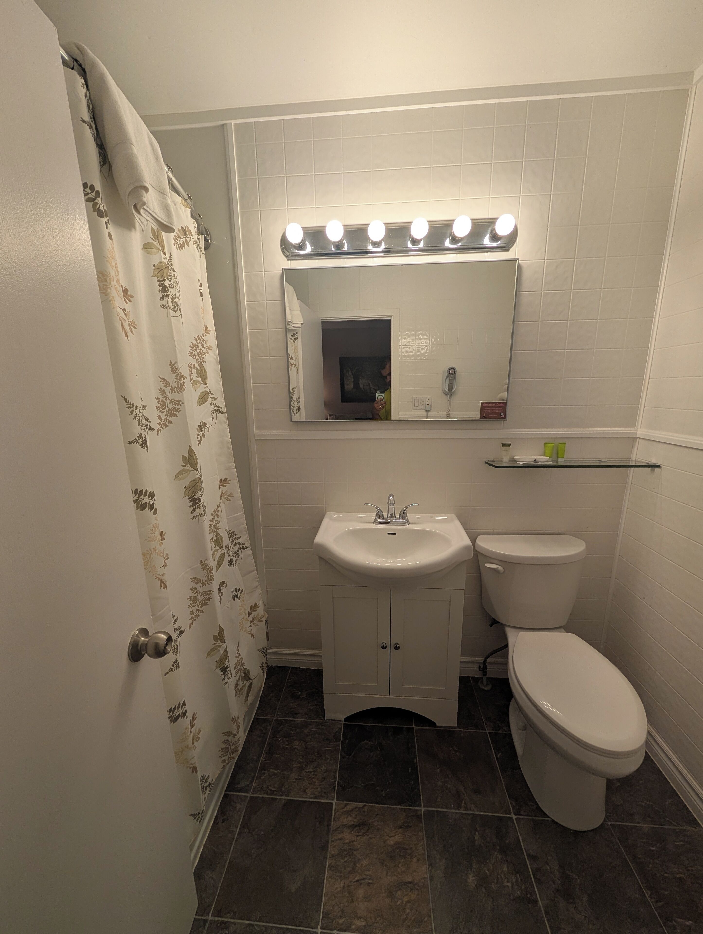 Un baño con lavamanos blanco, inodoro, espejo con luces y cortina de ducha.