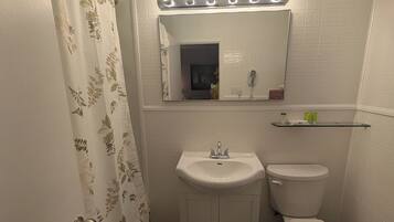 A bathroom with a white sink, a toilet, a mirror with lights, and a shower curtain.