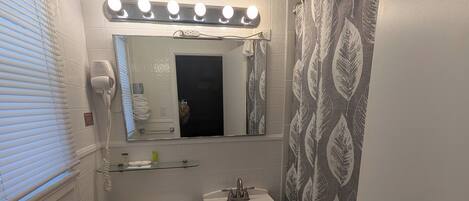 A bathroom with a toilet, sink, vanity, and a mirror with lights above.