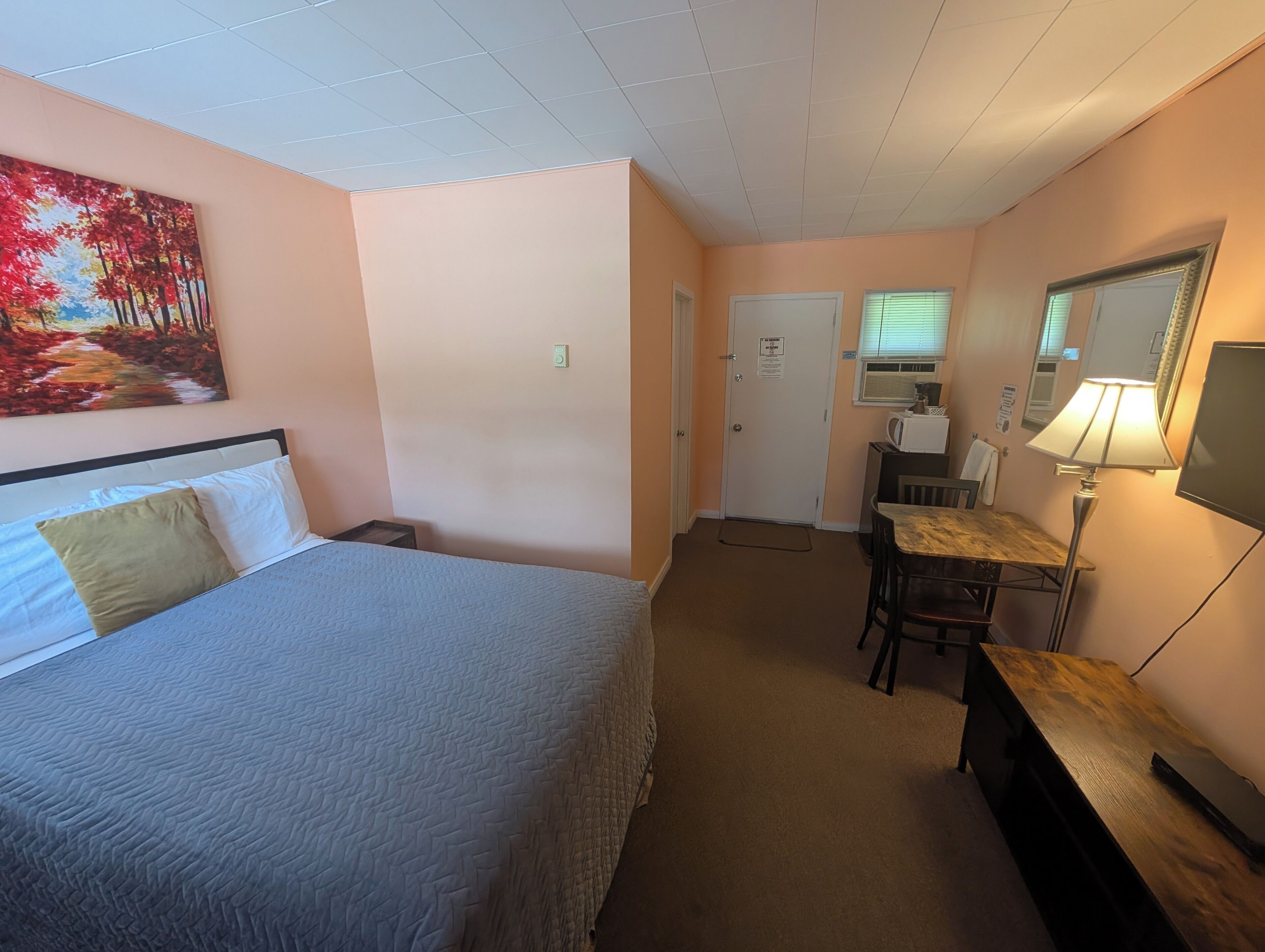 Een hotelkamer met een bed, een bureau, een stoel, een lamp, een televisie en een schilderij aan de muur.