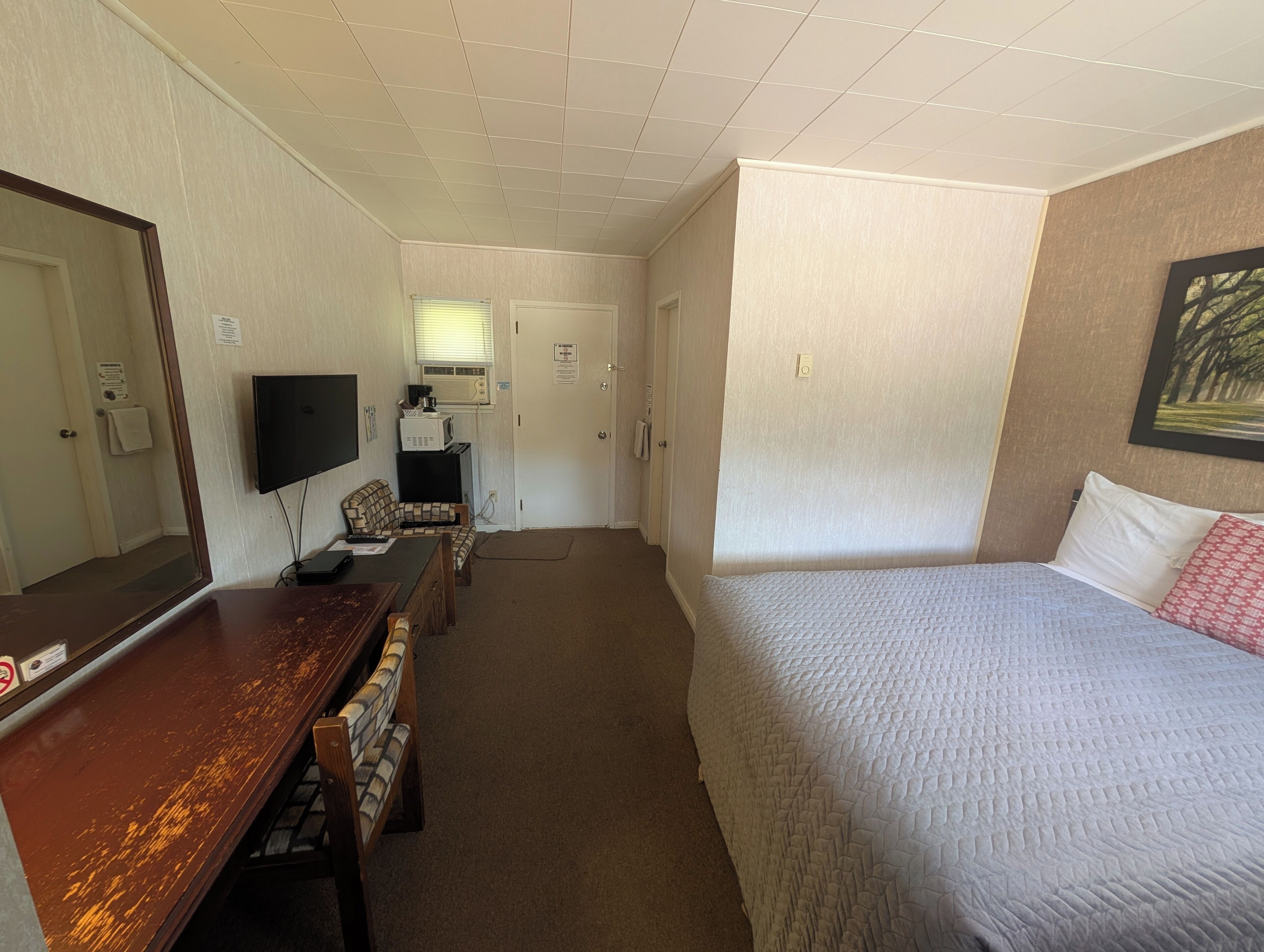 A hotel room with a bed, a desk with a chair, a television, and a window with blinds.