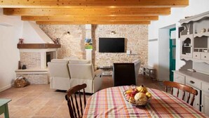 Una sala de estar acogedora con pared de piedra, chimenea, televisor y comedor con mesa preparada para cuatro.