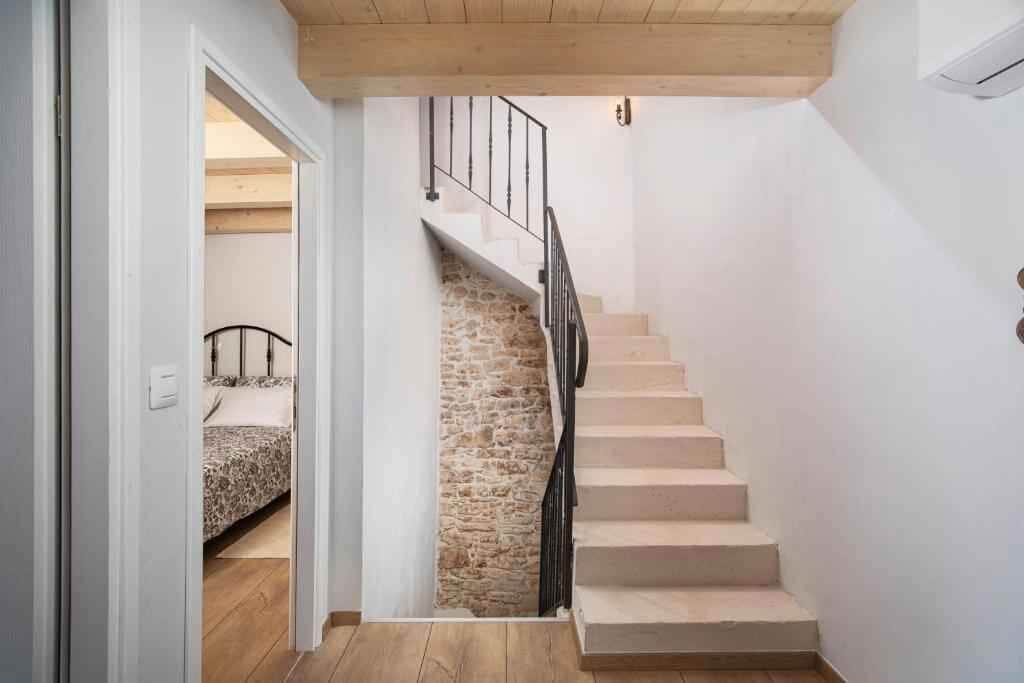 Eine Treppe mit einer Steinsäule auf einer Seite und einem Holzboden auf der anderen, die zu einem Schlafzimmer mit einem Bett und einem Nachttisch führt.