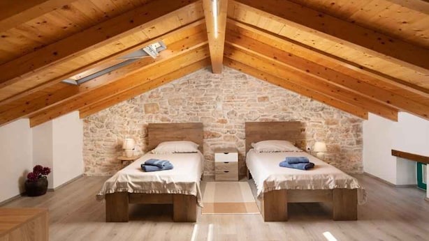 Un dormitorio acogedor en el ático con dos camas de madera, paredes de piedra y un techo inclinado de madera.