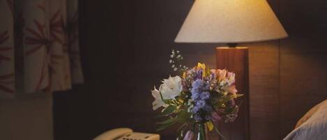 Habitación de hotel con una mesita de noche que incluye una lámpara, un teléfono y un arreglo floral.