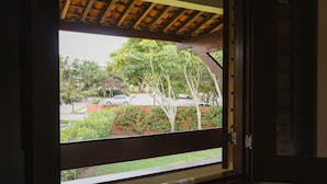 A window with a view of a parking area, trees, and a building in the background. - Hotel Fazenda Portal de Gravatá (Gravatá)