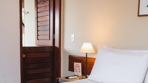 A hotel room with a wooden door, a bedside table with a lamp, and a bed with white bedding. - Hotel Fazenda Portal de Gravatá (Gravatá)