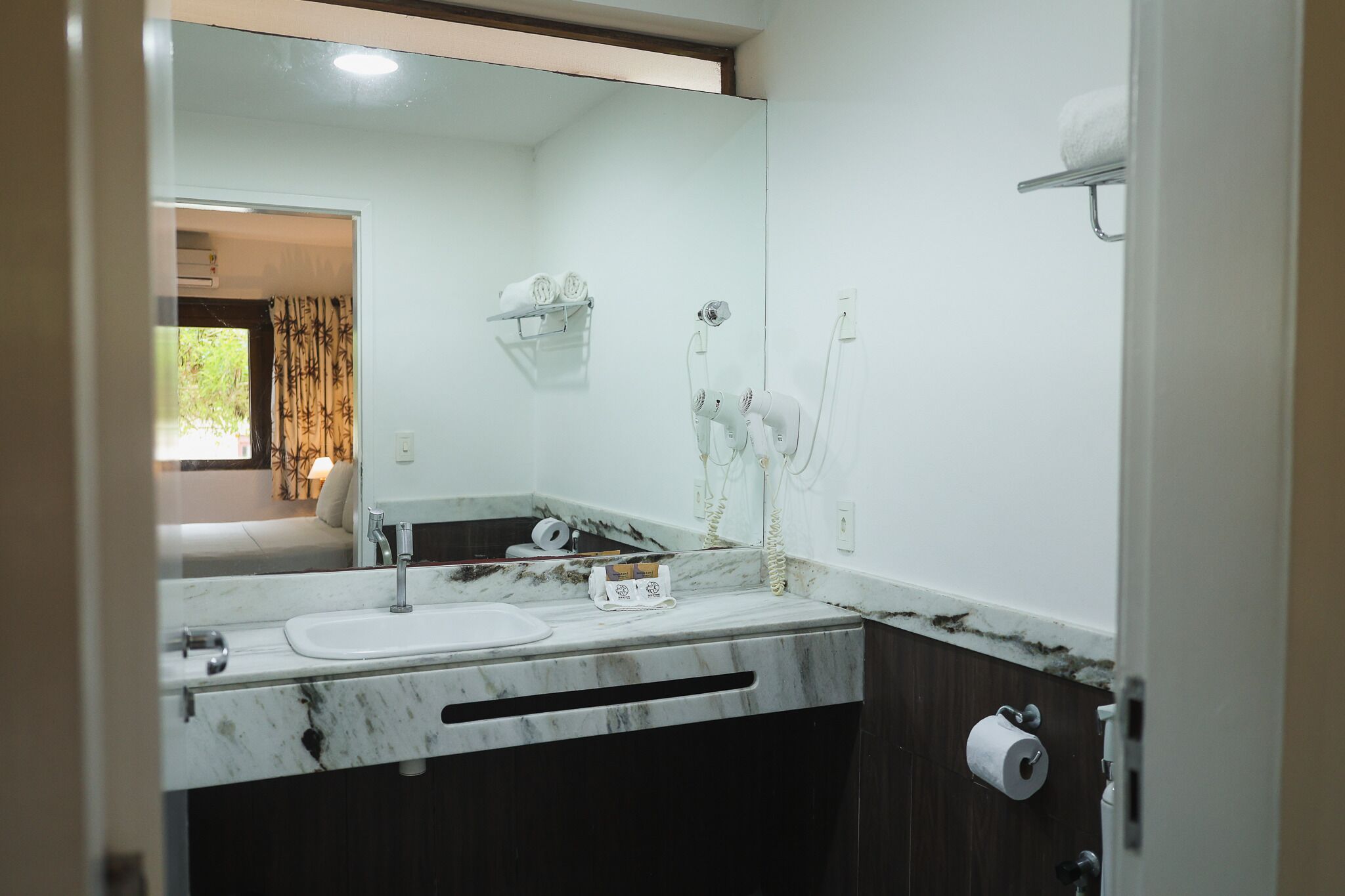 Un baño con lavamanos de mármol, un espejo grande, un perchero para toallas y un dispensador de papel higiénico.
