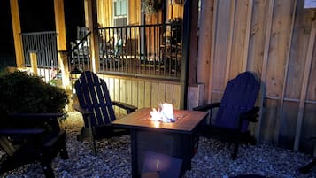 An outdoor seating area with Adirondack chairs and a fire pit, surrounded by a wooden deck and gravel.