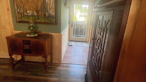 Un couloir au plancher de bois, une table à manger éclairée par une bougie, un tableau accroché au mur et, à travers une porte vitrée, une vue sur l’extérieur.
