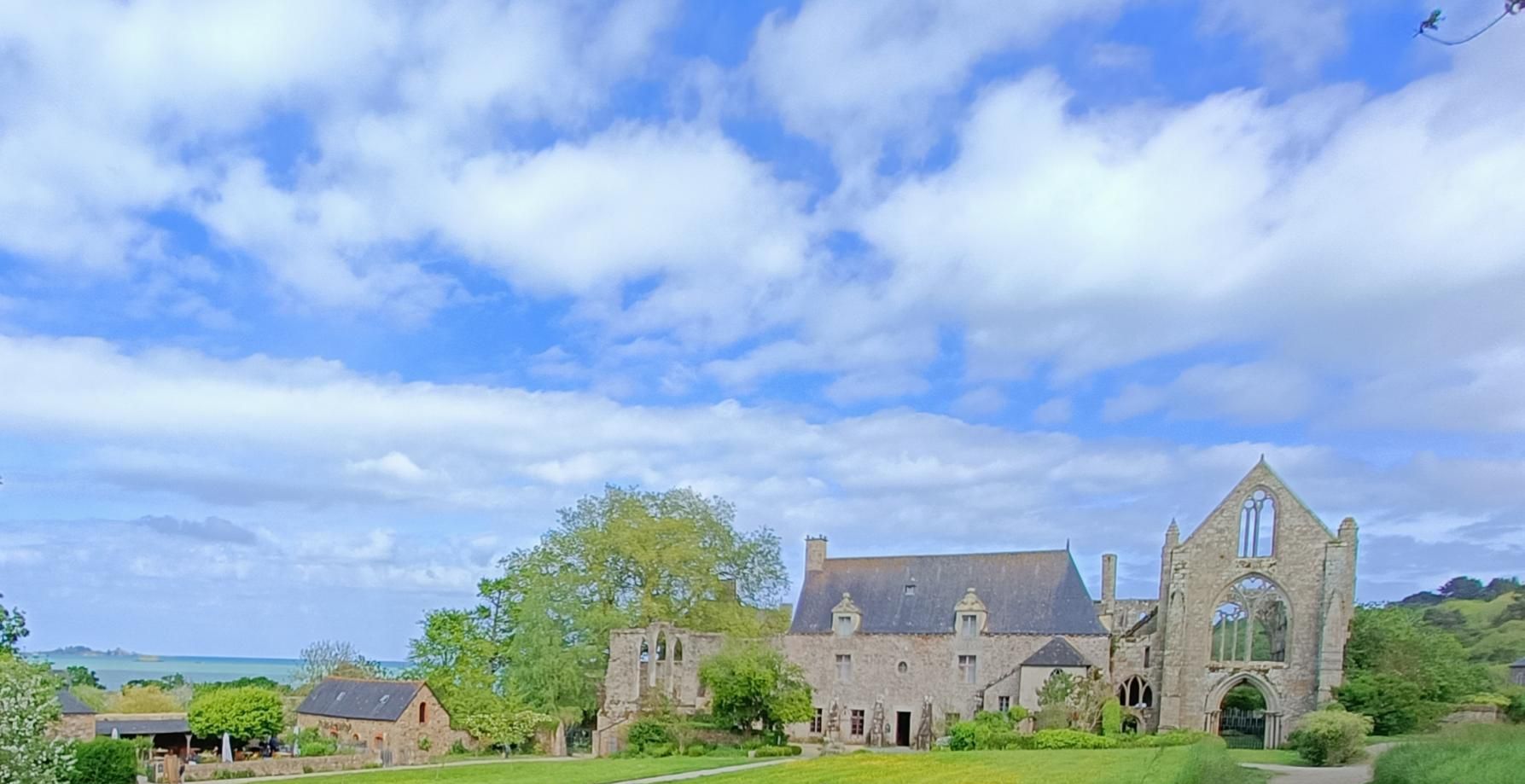 A historic abbey with a prominent church tower, surrounded by lush greenery and a clear sky.