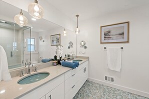Une salle de bain moderne avec deux vasques, un grand miroir et un tableau représentant un paysage, encadré.