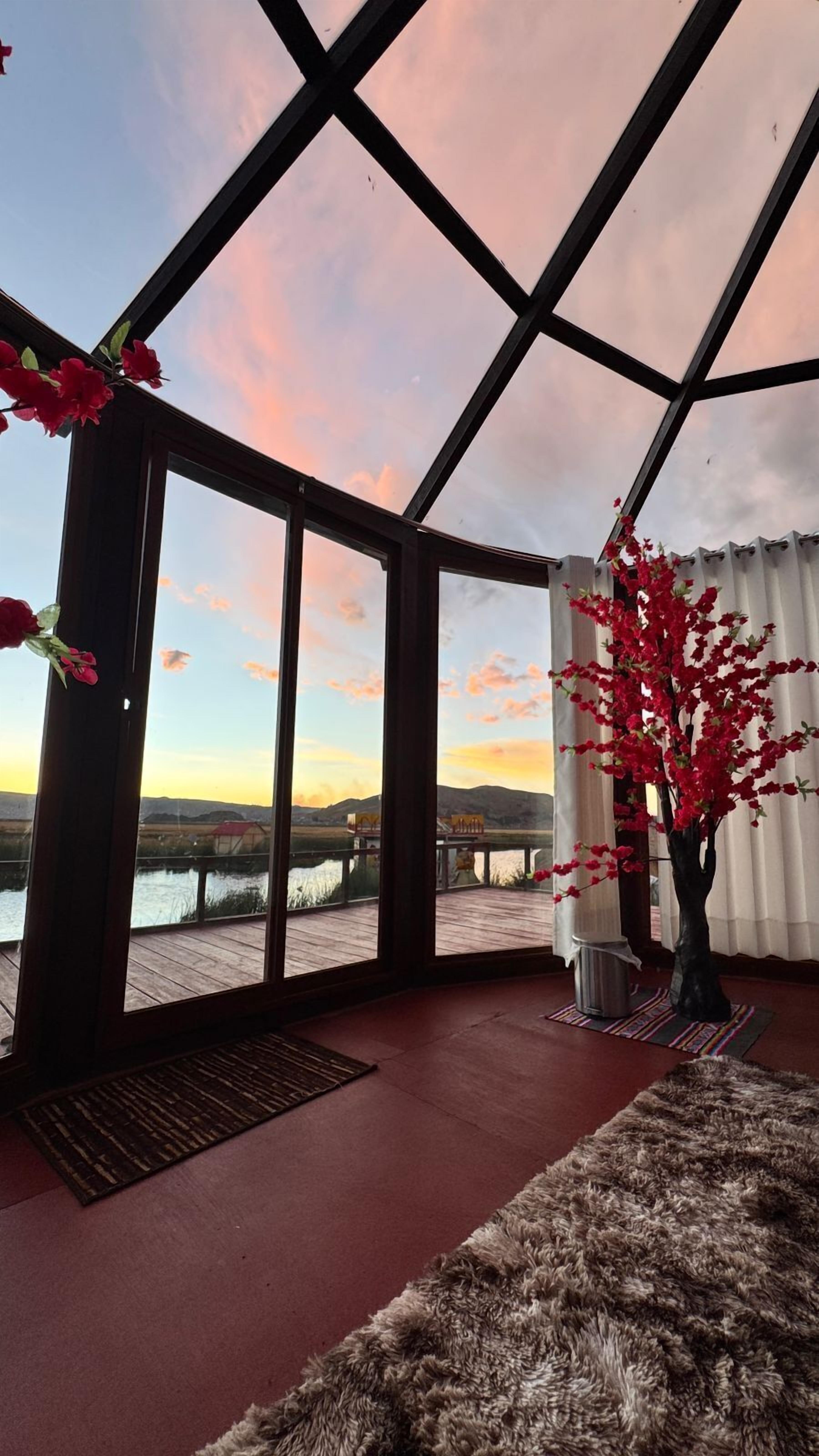 A room with large windows, a wooden floor, a fur rug, and a red flower arrangement.