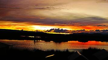 Un atardecer sobre un lago tranquilo con un muelle y montañas distantes.